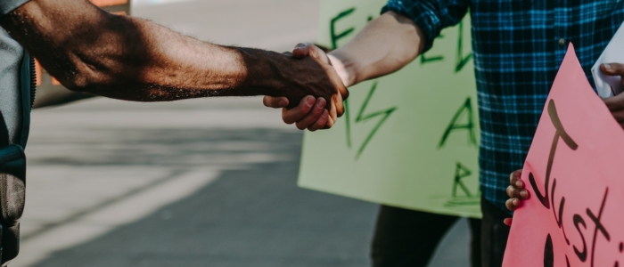 Two people extend their arms to shake hands at a protest.
