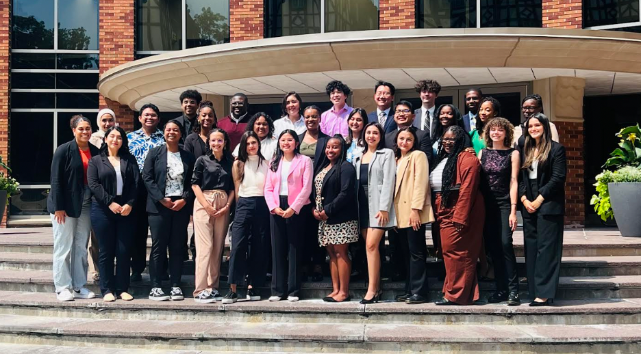 Group photo of the 2023 Future Public Health Leaders Program cohort. About 30 people wearing professional attire are smiling and standing in front of the entrance to a building.