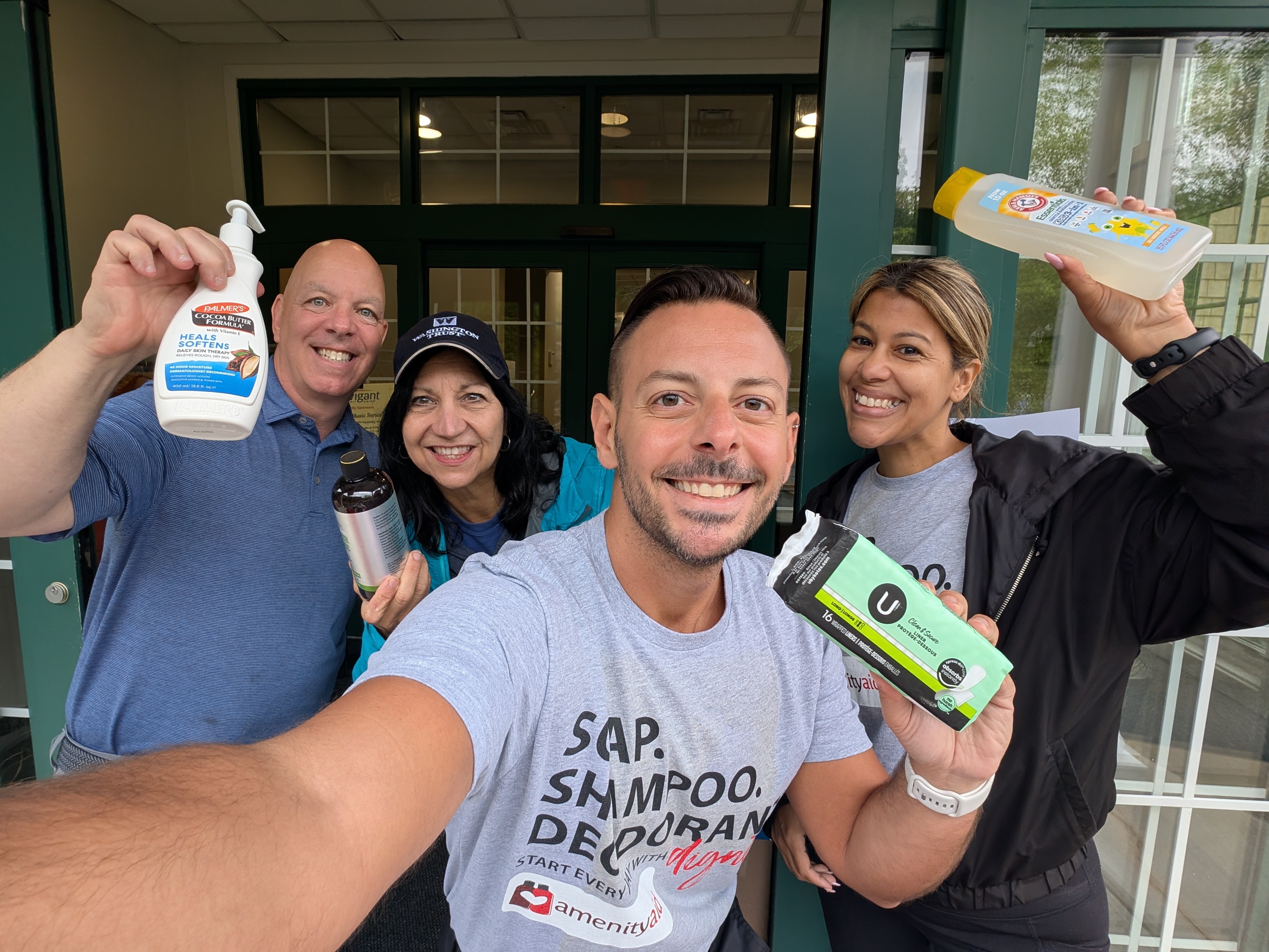 Four smiling people pose for a selfie while holding personal hygiene products.